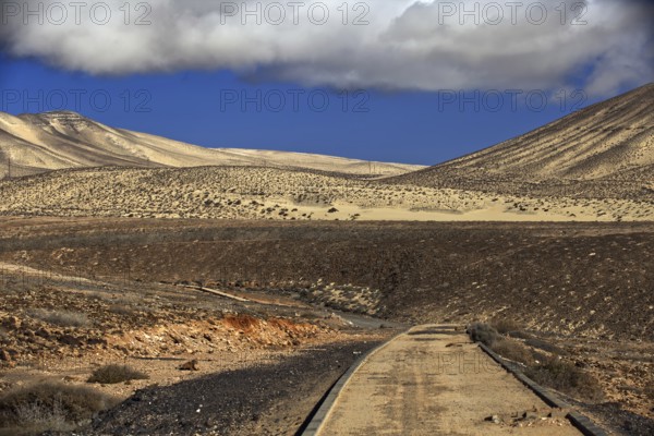 Lonely road in front of a dune landscape under a cloudy sky, Pajara, Fuerteventura, Canary Islands, Spain, Europe