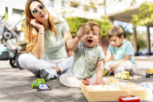 Baby holding a toy and laughing next to his family playing together on an urban park