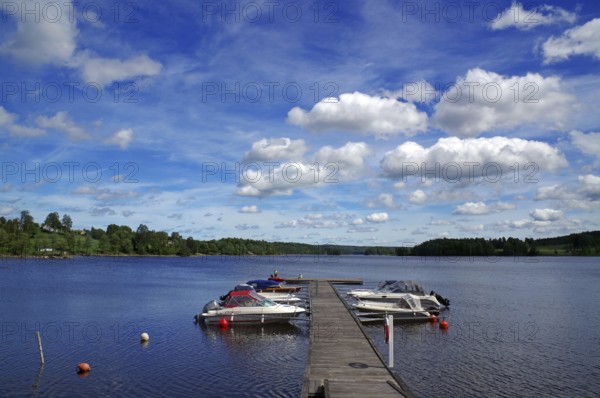 Lake with a wooden jetty and boats moored on it under a blue sky with white clouds, Stora Le, Nössemark, Dalslan Canal, Sweden, Europe