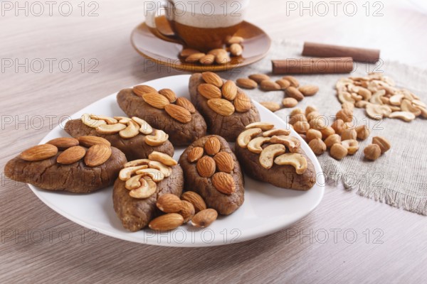 Small cakes potatoes with almonds and cashew nuts on a dessert plate. A cup of coffee, cinnamon, almonds, hazelnuts, cashew on a linen napkin. Still life. Copy space