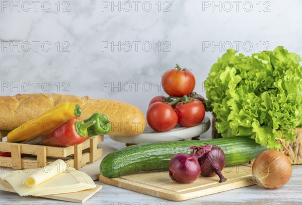 Colourful peppers, tomatoes, cucumber, lettuce and slices of cheese next to a baguette on a table, copy room