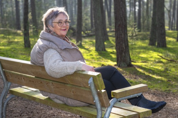 Elderly woman, 65 years old, sitting on a bench and enjoying nature in the forest in Ystad, Skåne, Sweden, Scandinavia, Europe