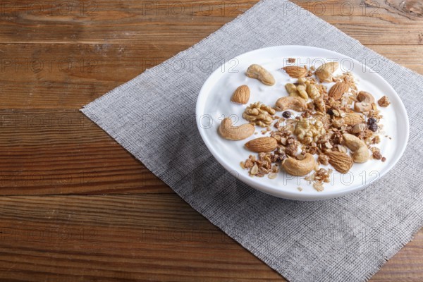 White plate with greek yogurt, granola, almond, cashew, walnuts on brown wooden background. close up. copy space