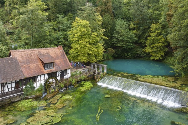 Blautopf Blaubeuren with industrial monument Hammerschmiede, source of the little river Blau in a landscape with forest. Karst spring, geotope and geopoint of the UNESCO Swabian Alb Geopark, tourist attraction. The popular excursion destination is now being thoroughly renovated and will therefore be closed to visitors until the end of 2028. Drone photo. Blaubeuren, Baden-Württemberg, Germany, Europe