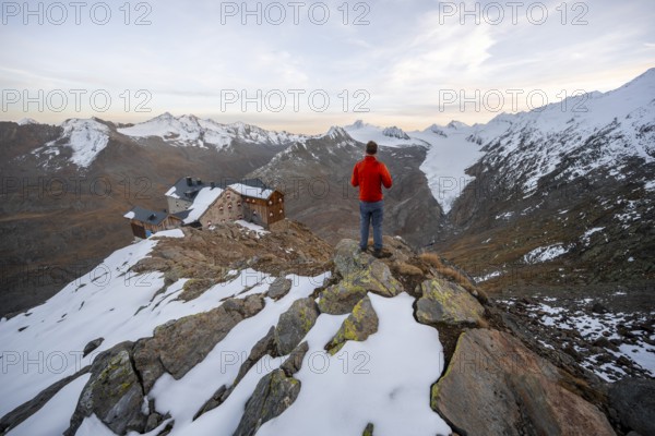 Hiker looking at mountain panorama and glacier, mountain hut Ramolhaus in autumn with snow, at sunset, view of Gurgler Ferner with summit Hochwilde and Falschungsspitze, Ötztal Alps, Tyrol, Austria, Europe