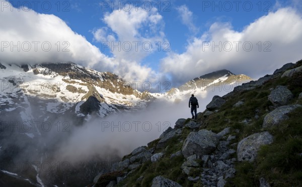 Silhouette of a mountaineer in front of a cloudy, atmospheric mountain landscape, rocky snow-covered mountains with summit Hochsteller, Furtschaglhaus, Berliner Höhenweg, Zillertal Alps, Tyrol, Austria, Europe
