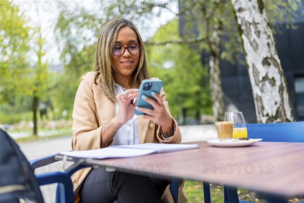 Relaxed beauty latin businesswoman using mobile sitting on an outside cafeteria