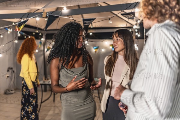 Multi-ethnic young people in elegant clothes chatting during night party at terrace