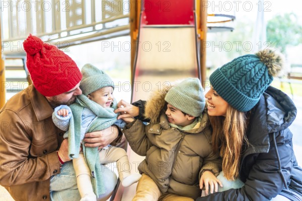 Cheerful family bundled in winter clothes enjoying quality time together while sliding down a playground slide, creating joyful memories