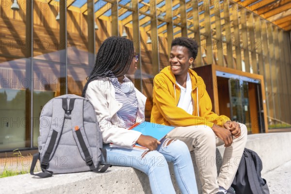 Two male and female african students talking sitting together in the university campus in a sunny day