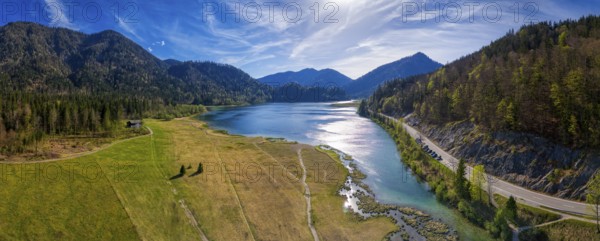 Picturesque panorama of a mountain lake with wooded hills and a road along the shore under a blue sky, Weitsee