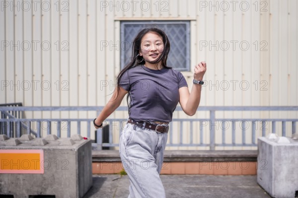 Asian woman dancing energetically k-pop style dance outside an industrial building