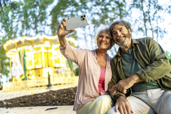 Senior couple taking selfie sitting on bench in a night city fair