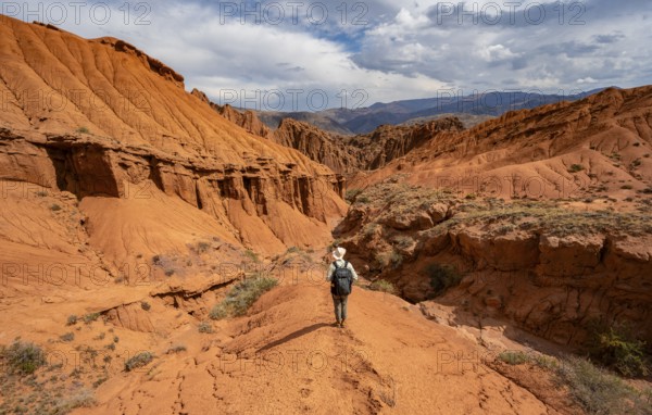Mountaineer on a mountain ridge, view of eroded mountain landscape with sandstone cliffs, canyon with red and orange rock formations, Konorchek Canyon, Chuy, Kyrgyzstan, Asia