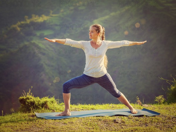 Yoga outdoors, sporty fit woman doing yoga asana Virabhadrasana 2, Warrior pose posture outdoors in Himalayas mountains in the morning. Vintage retro effect filtered hipster style image