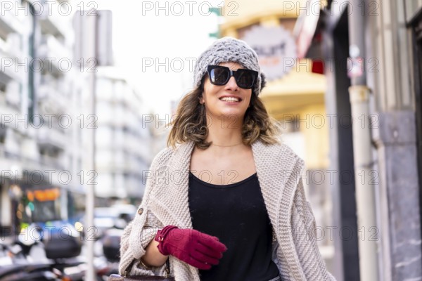 Lifestyle, young Caucasian blonde girl enjoying and smiling in the city in winter. Strolling with sunglasses and red gloves