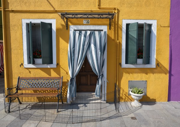 Yellow house facade with entrance door with green and white curtain and windows, colourful houses on the island of Burano, Venice, Veneto, Italy, Europe
