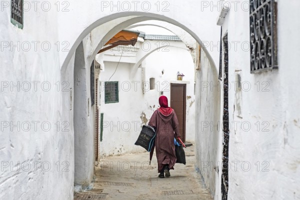 Moroccan Muslim woman in traditional Islamic dress wearing hijab walking with shopping bags in medina of the city Tétouan, Tettawen, Morocco, Africa