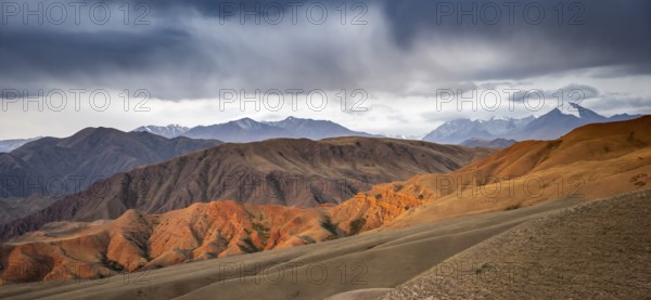 View over eroded mountainous landscape of Konorchek Canyon with red sandstone cliffs, high mountains with snow behind, dramatic dark clouds, Konorchek Canyon, Chuy, Kyrgyzstan, Asia