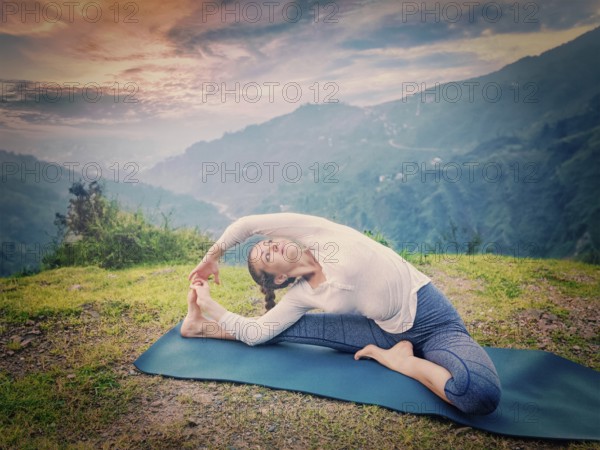 Yoga outdoors, young sporty fit woman doing Hatha Yoga asana janu sirsasana, Revolved Head-to-Knee Pose, in. Vintage retro effect filtered hipster style image