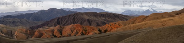 Panorama, view over eroded mountainous landscape of Konorchek Canyon with red sandstone cliffs, high mountains with snow in the background, dramatic dark clouds, Konorchek Canyon, Chuy, Kyrgyzstan, Asia