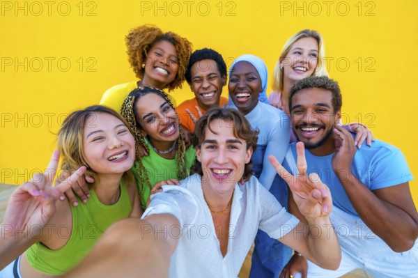 Multi-ethnic friends gesturing success while taking a selfie next to a yellow wall