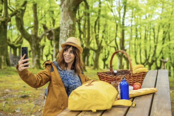 A young Caucasian woman waving on the phone sitting at a picnic table in the woods. Summer lifestyle