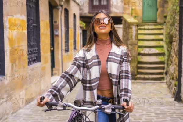 Pretty latin woman with sunglasses doing bicycle sightseeing in the city through the old town. Eco tourism in spring on vacation, model smiling