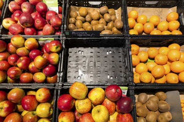Fruit counter in a supermarket or organic food shop, here with different types of apples, kiwis, oranges and an empty compartment for pears