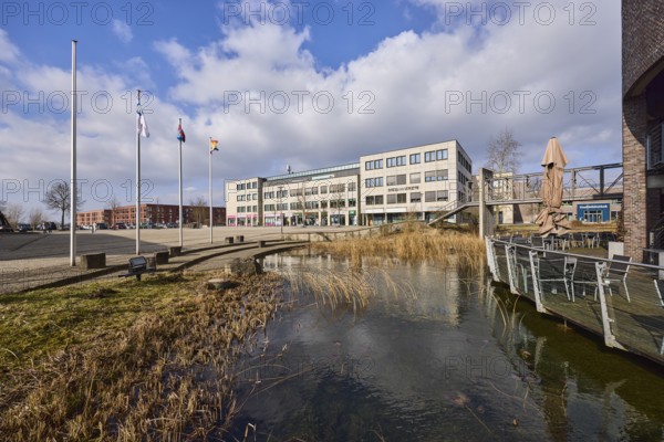 Rathausterassen Garbsen, outdoor area of a restaurant, pond, lawn, flagpoles, commercial buildings, city trees, blue sky with cumulus clouds, town hall square, Garbsen, Hanover region, Lower Saxony, Germany, Europe