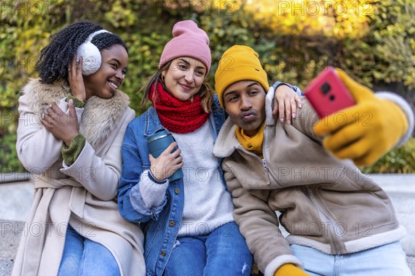 Three young friends wearing winter clothes taking a selfie with smartphone in a city park