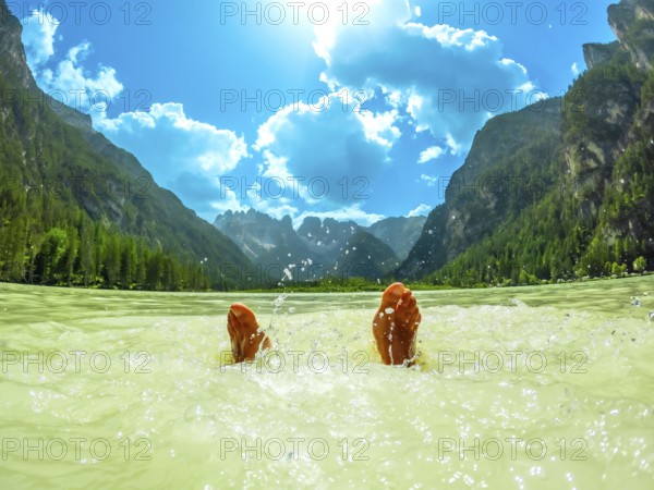 Feet splashing in the water of a mountain lake in the italian dolomites during summer, with a breathtaking view of the surrounding peaks