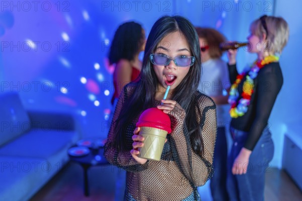 Asian woman drinking a colorful beverage at a lively party with friends, enjoying the music and atmosphere