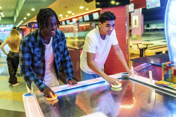 Two young men concentrating on playing air hockey in a vibrant entertainment center, enjoying a friendly competition