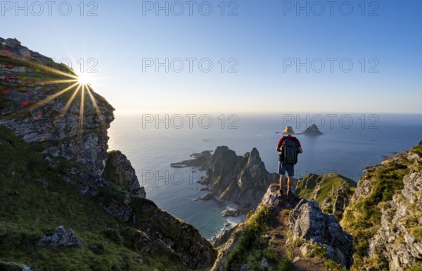 Mountaineer on the summit of Måtind or Måtinden, view of picturesque coastal landscape with sun star, rocky coast and sea, Andøya Island, Vesterålen, Nordland, Norway, Europe
