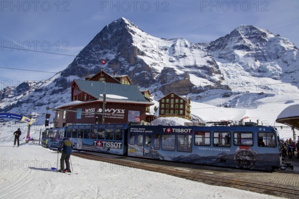 25 March 2024, Kleine Scheidegg, Grindelwald Switzerland : Many skiers and tourists enjoy the sunny winter weather. In the background the famous north face of the Eiger, in the foreground the Wengernalp railway, the longest cog railway in the world
