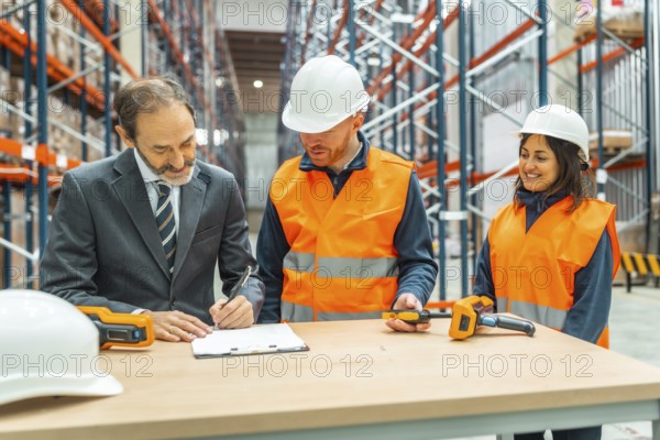 Manager signing delivery notes in a logistics warehouse, assisted by two warehouse workers using barcode readers