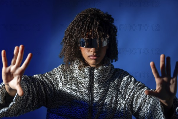 Young woman with futuristic visor and patterned jacket pushing virtual screen on blue background