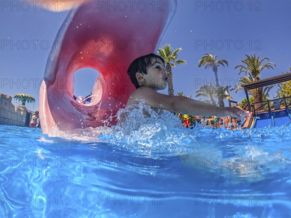 Young boy sliding joyfully into a pool at a vibrant water park, delighting in the excitement of summer vacation and playful splashes