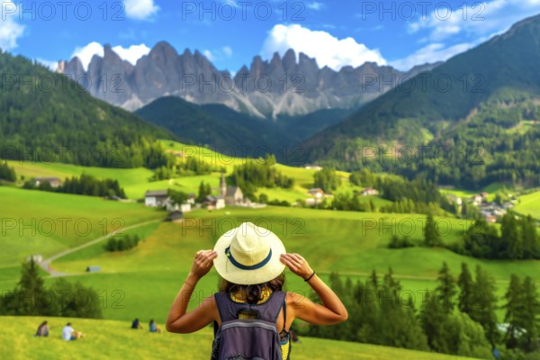 Female tourist holding her hat while looking at st. Magdalena church in val di funes with the odle mountains in the background