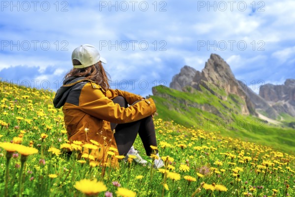 Female hiker enjoying the breathtaking view of the seceda mountain range in the dolomites, italy, surrounded by vibrant wildflowers