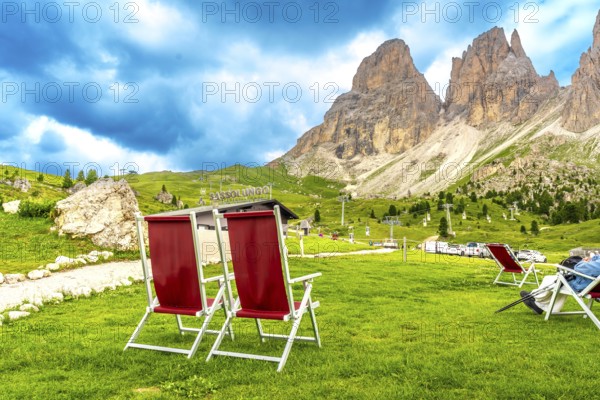 Red deckchairs inviting tourists to relax and enjoy the breathtaking view of the sassolungo mountain in the dolomites during summer