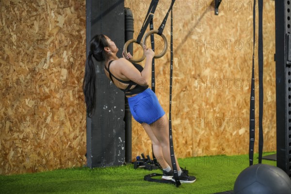 Full length side view of an asian woman exercising using gym rings to do pull-ups