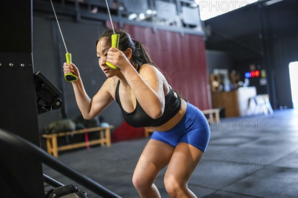 Chinese woman using lat machine to pull weights in a cross training modern gym