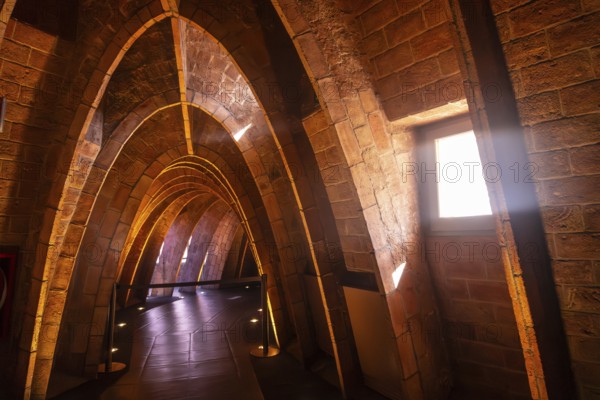 Warm sunlight streams through a window, illuminating the unique brick arches in the attic of casa mila, a famous architectural landmark in barcelona, spain