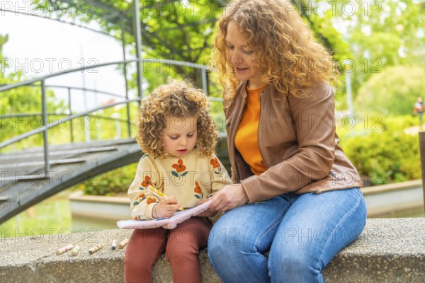 Blonde caucasian little girl learning to read on a park sitting with her mother