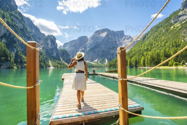 Woman walking along a wooden pier at lake braies, enjoying the turquoise waters and stunning mountain landscape of the dolomites on a sunny summer day