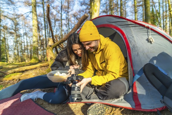 Couple enjoying a moment together while reviewing mushroom photos on a digital camera during a camping trip in the serene forest