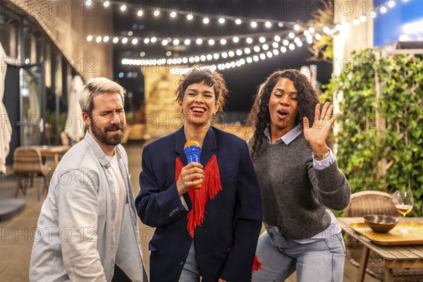Happy diverse friends dancing and singing karaoke at night party in the roof terrace of an urban bar
