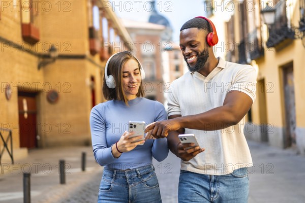 Happy multi-ethnic couple listening to music and using mobile phone walking in the city